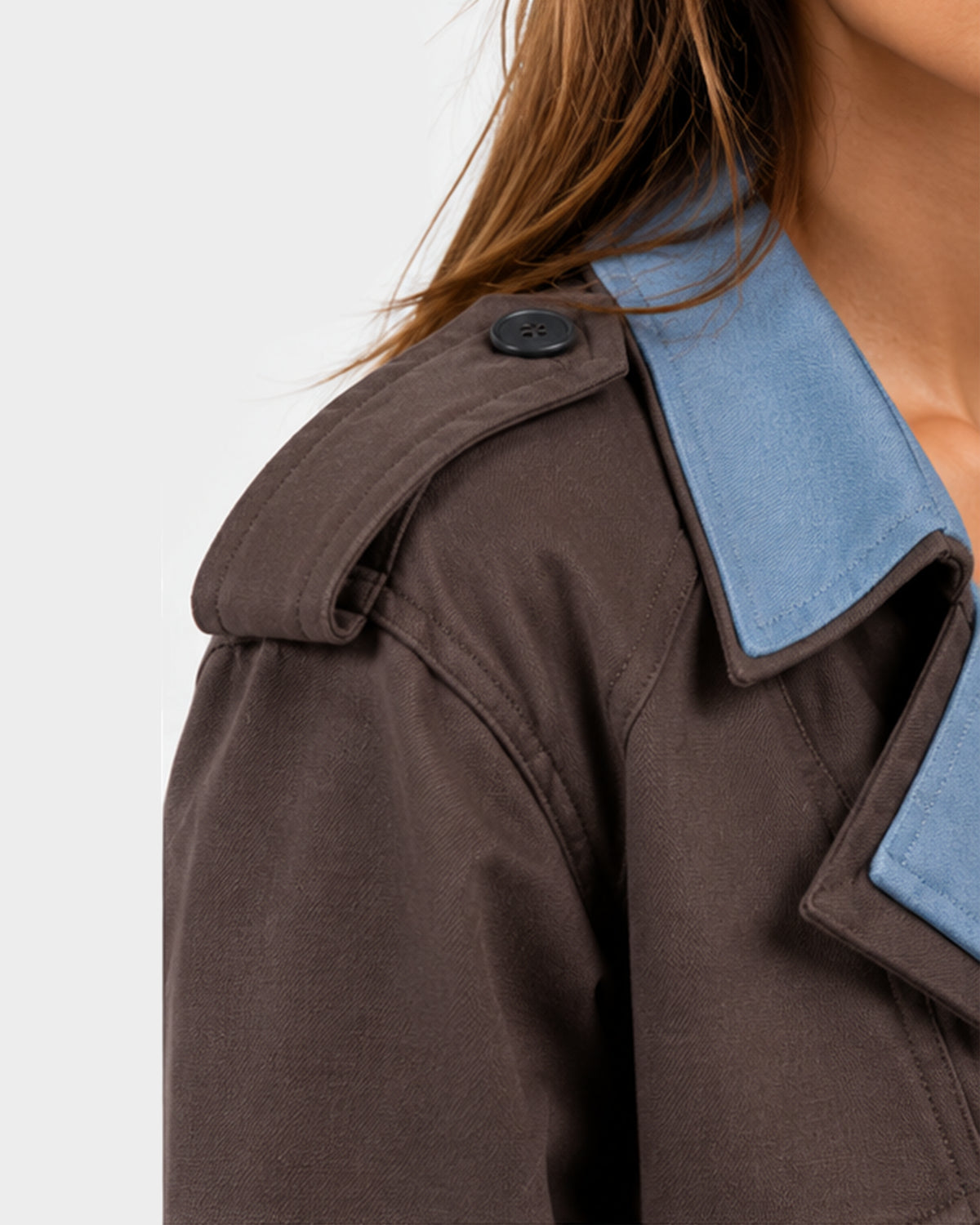 Close-up of a person wearing a dark brown jacket with a contrasting light blue collar, showing the shoulder detail and button.