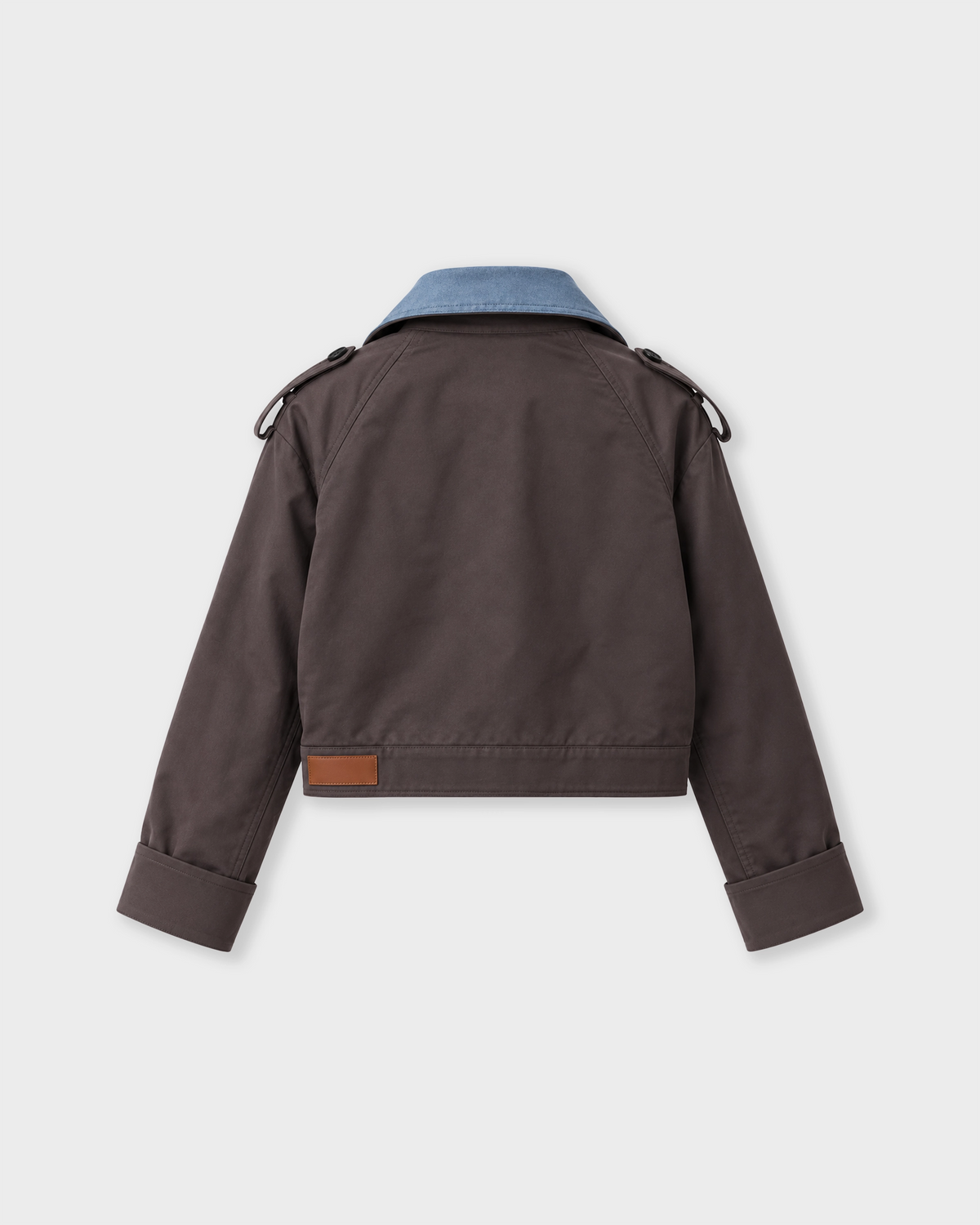 A dark brown cropped jacket shown from the back, featuring a light blue denim collar, shoulder epaulets with drawstrings, and a small brown leather patch near the hem, displayed on a light gray background.
